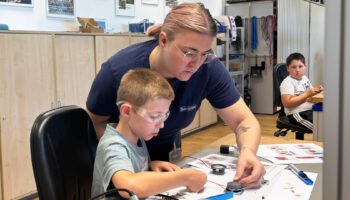 Pictured are a woman and a young boy. The woman is helping the boy
