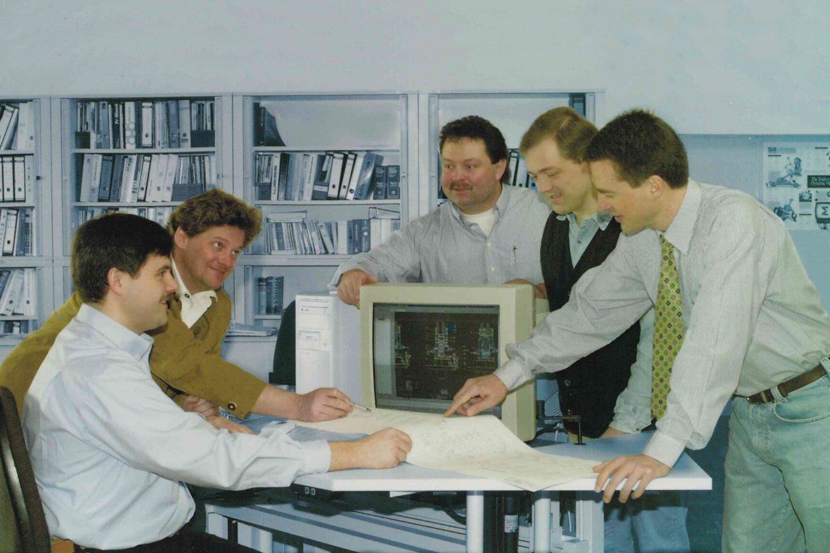 Auf dem historischen Foto sind die fünf Gründer von Sonplas um einen Bildschirm und Konstruktionszeichnungen versammelt.