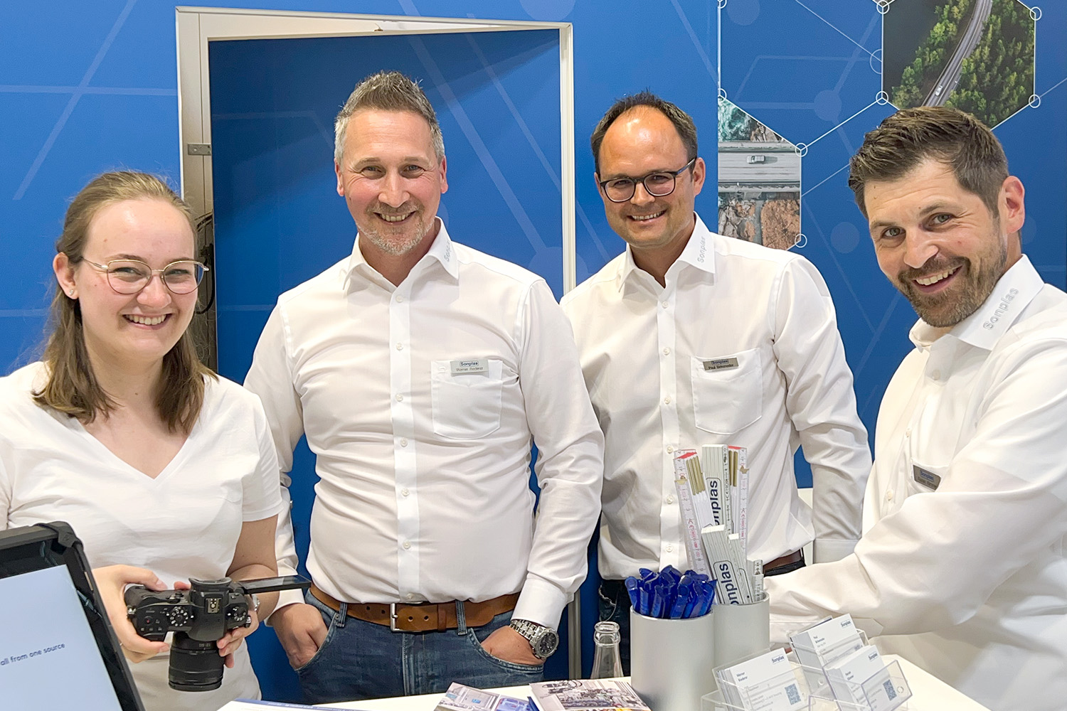 Eine Frau und drei Männer stehen nebeneinander auf einem Sonplas-Messestand und lachen in die Kamera.
