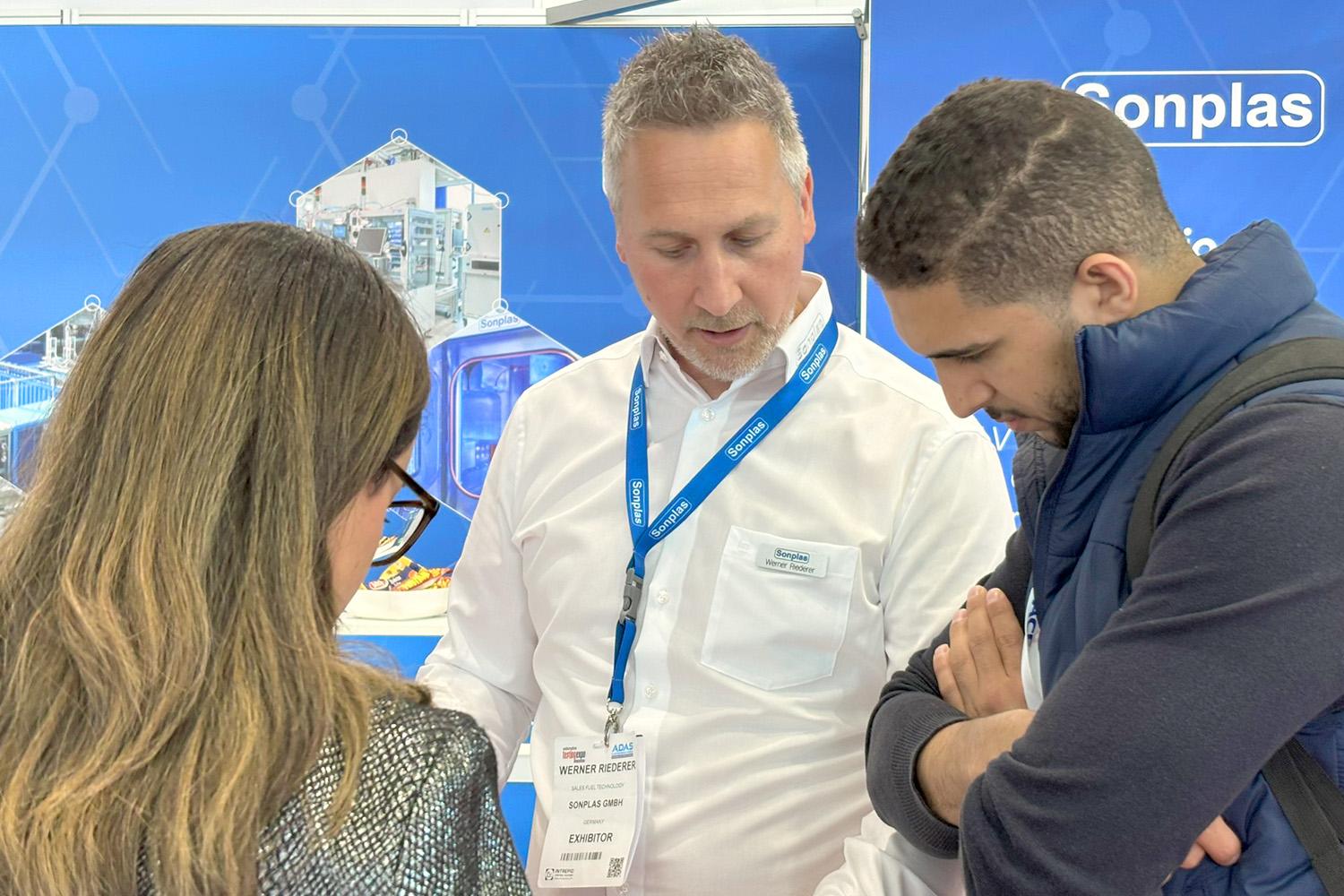 Ein Sonplas Mitarbeiter unterhält sich mit zwei Besuchenden auf einem Sonplas-Messestand