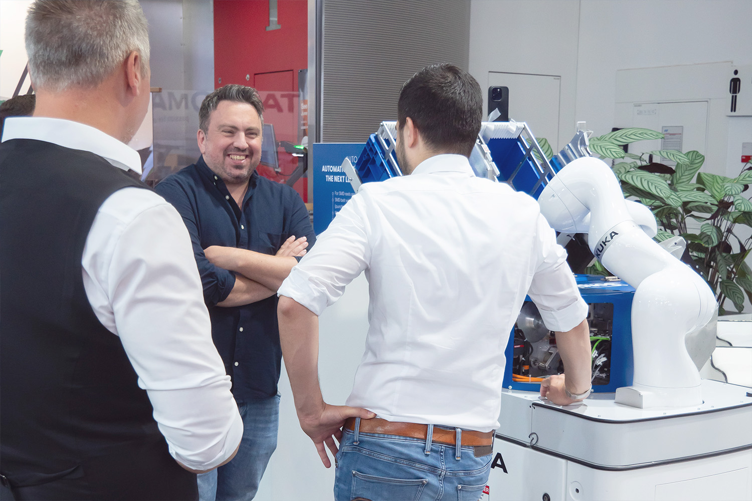 Zwei Sonplas-Mitarbeitende unterhalten sich mit einem Standbesucher am Sonplas-Messestand. Der Besucher lacht.