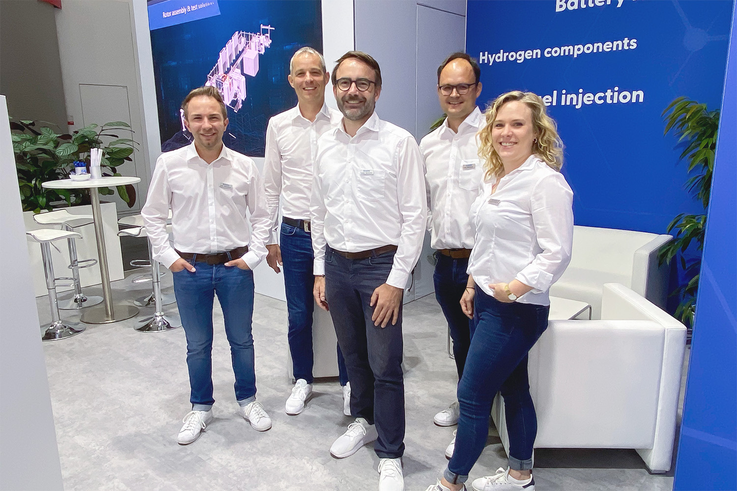 Gruppenbild mit Sonplas-Mitarbeitenden auf einem Messestand. Vier Mitarbeiter und eine Mitarbeiterin lachen freundlich in die Kamera, im Hintergrund bekommt man Einblicke in den Messestand.